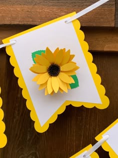 a paper sunflower is hanging from a string on a wooden table with white and yellow cards