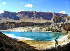 two people riding bikes on the side of a mountain with a lake and mountains in the background