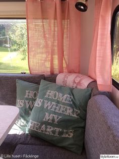 a couch with two pillows on top of it in front of a window that says home is where my heart is