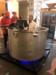 two men standing in front of a large metal pot with laptops on top of it