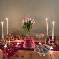 a table topped with lots of pink and white cake next to candles on top of a wooden table