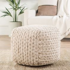 a living room with a white couch and large knitted ottoman on the floor next to a potted plant