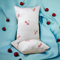 a white pillow with cherries on it next to a blue sheet and cherry pillows