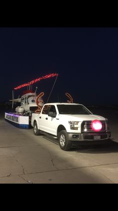 a white truck pulling a trailer with an airplane on it's flatbed at night