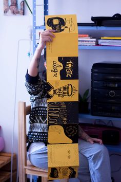 a person sitting in a chair holding up a yellow skateboard with pictures on it