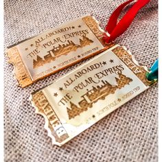 two gold tickets with red ribbon on the top and bottom are sitting on a white cloth