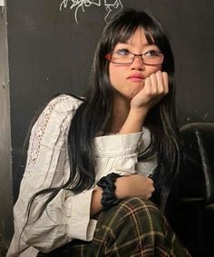 a woman with glasses sitting in front of a blackboard and writing on the wall