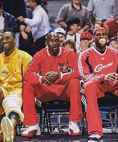 three basketball players sitting on the sidelines in front of an audience at a game