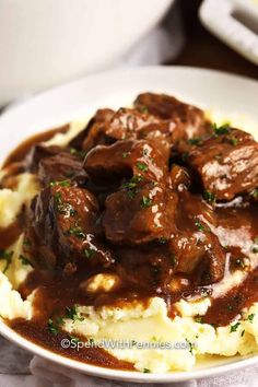 a white plate topped with mashed potatoes and meat covered in gravy on top of a wooden table