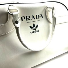 About This Bag: Limited Edition #117/700. Prada X Adidas Shoulder Bag White Leather Graphic Print Silver-Tone Hardware Rolled Handles & Single Adjustable Shoulder Strap Canvas Lining & Dual Interior Pockets Zip Closure At Top Protective Feet At Base Includes Box & Dust Bag Condition: Minor Marking At Exterior. Estimated Item Measurements Shoulder Strap Length: 34.75" Shoulder Strap Drop Max: 20.5" Shoulder Strap Drop Min: 11.5" Handle Drop: 6.5" Height: 12.25" Width: 18.75" Depth: 9" Adidas Bag, Adidas Bags, Bowling Bag, Bowling Bags, White Bag, Bowling, Limited Editions, White Leather, Graphic Prints