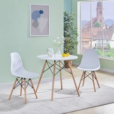 two white chairs sitting at a table in front of a window next to a potted plant