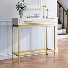 a white and gold console table with flowers on it in front of a stair case