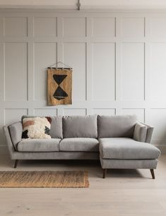 a living room with a gray couch and rugs on the floor, white paneled walls