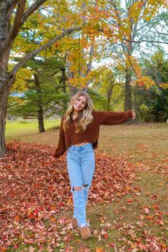 a woman standing in the leaves with her arms outstretched