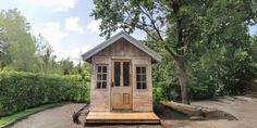 a small wooden outhouse sitting on top of a dirt field next to a tree