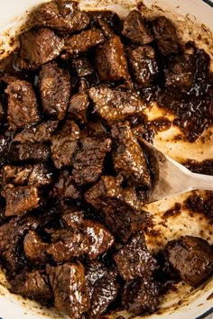 a pot filled with meat and sauce on top of a stove next to a wooden spoon