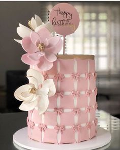 a pink and white birthday cake with flowers on it's top, sitting on a table