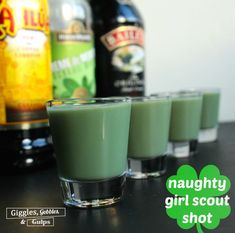 three shot glasses filled with green liquid next to bottles