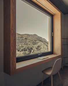 a window that has a view of the mountains out to the field below it, with a chair in front of it