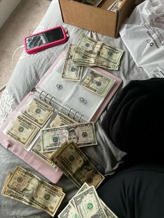 a pile of money sitting on top of a bed next to a box with a cell phone