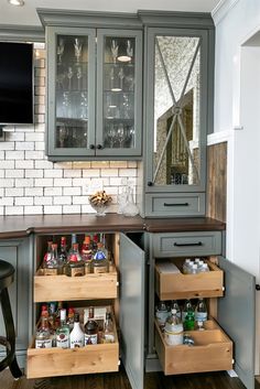 an open cabinet in the corner of a kitchen with wine glasses and liquor bottles on it