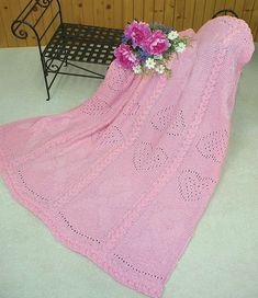 a pink crocheted blanket sitting on top of a table next to a bench