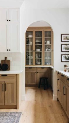 a kitchen with white walls and wooden cabinets in the center is an arched doorway leading to another room