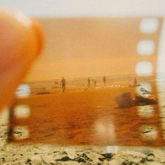 a hand holding up a polaroid with people walking on the beach in the background