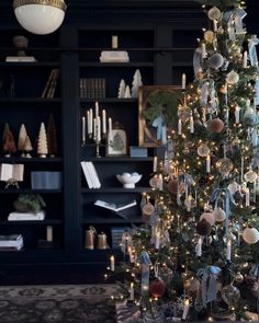 a decorated christmas tree in front of a book shelf with candles and ornaments on it