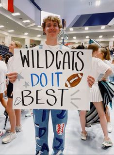 a man holding a sign that says wildcats do it best with footballs on it