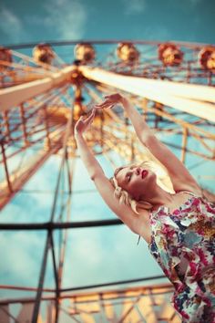 a woman standing in front of a ferris wheel with her arms stretched out to the side