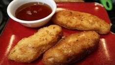 three fried fish sticks on a red plate with dipping sauce