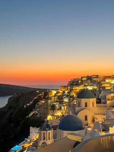 the sun is setting over some white buildings and blue domes in front of an ocean