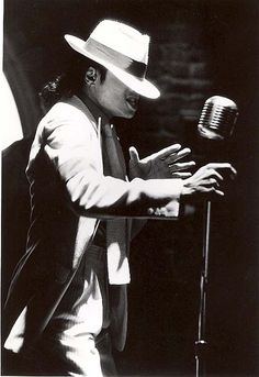 a man wearing a hat and holding a microphone in front of a microphone with his hands out