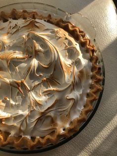 a pie with white frosting on top sitting on a table next to a window