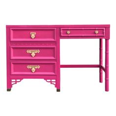 a pink desk with three drawers and gold pulls on the top, against a white background