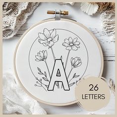 an embroidery kit with flowers and the letter a in it's center, on top of