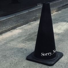 a black cone sitting on the side of a road next to a street sign that says sorry, no