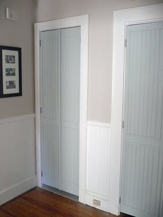 two white doors in a room with wood flooring and framed pictures on the wall