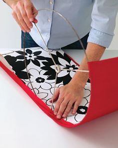 a woman cutting fabric with scissors on top of a piece of red material that has black and white designs