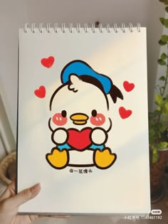 a hand holding up a drawing of a cartoon penguin with hearts on it's chest