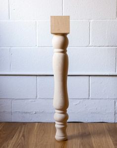 a wooden candle holder sitting on top of a hard wood floor next to a white brick wall