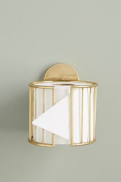 a white napkin holder with a gold finish on a gray wall next to a paper towel dispenser