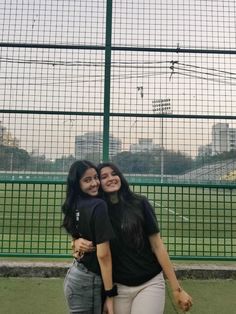 two young women standing next to each other in front of a tennis court with the city behind them