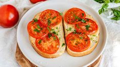 two slices of bread topped with tomatoes on top of a white plate next to fresh vegetables