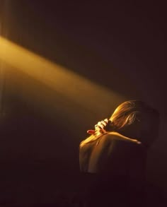 a woman is standing in the dark with her head turned to the side and light coming from behind her