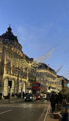 people are walking down the street in front of buildings with christmas lights strung across them