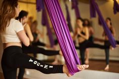 a group of women doing yoga exercises in a room with purple curtains hanging from the ceiling