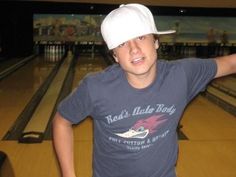 a young boy wearing a white hat standing in front of bowling lanes with his arms behind his head