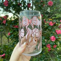 a hand holding up a glass with pink flowers on it